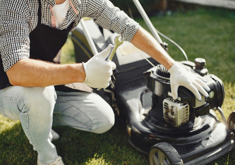“Man wearing a black apron mowing grass with a lawn mower in his backyard”
