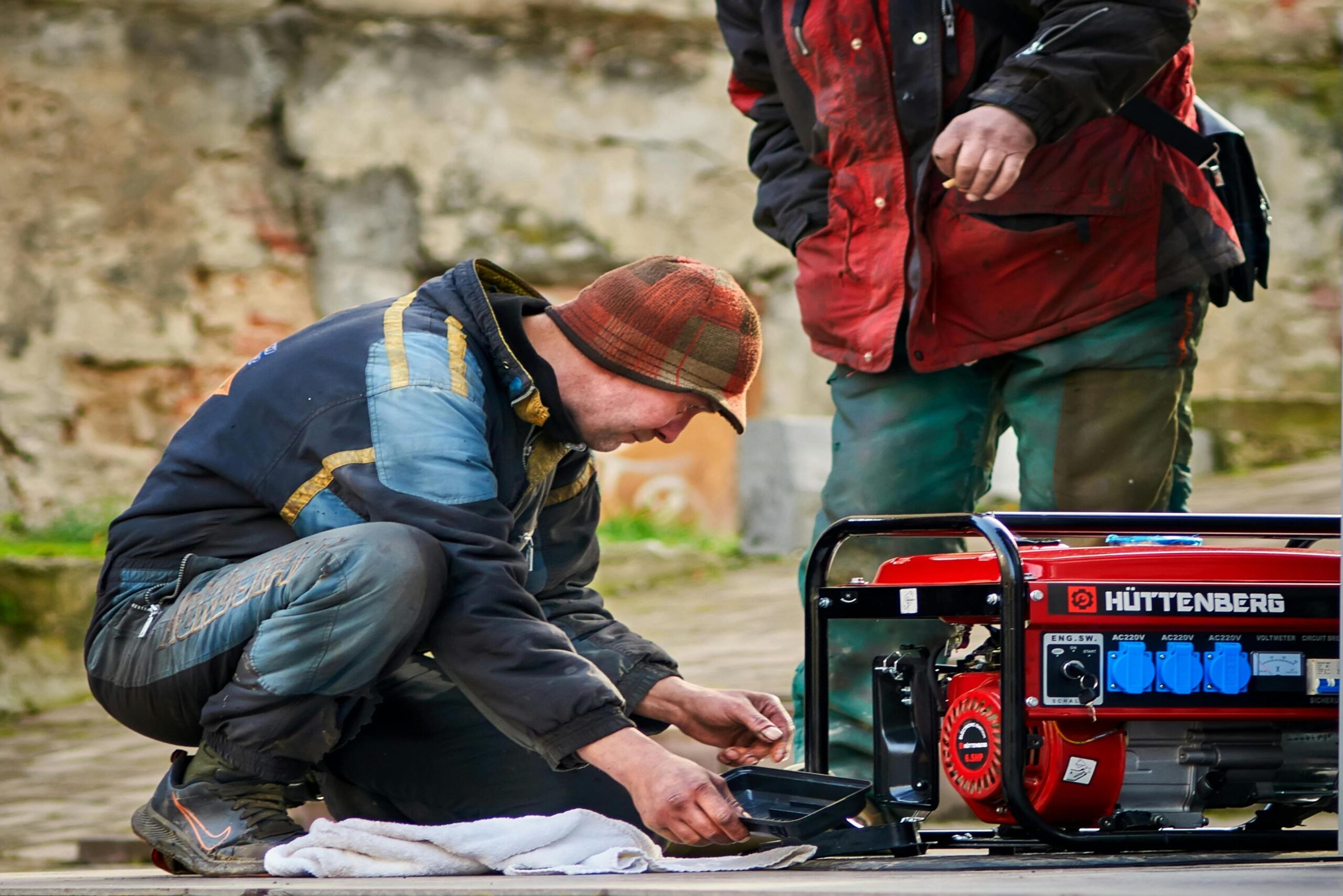 “Worker kneeling on grass and repairing a red lawn mower engine”
