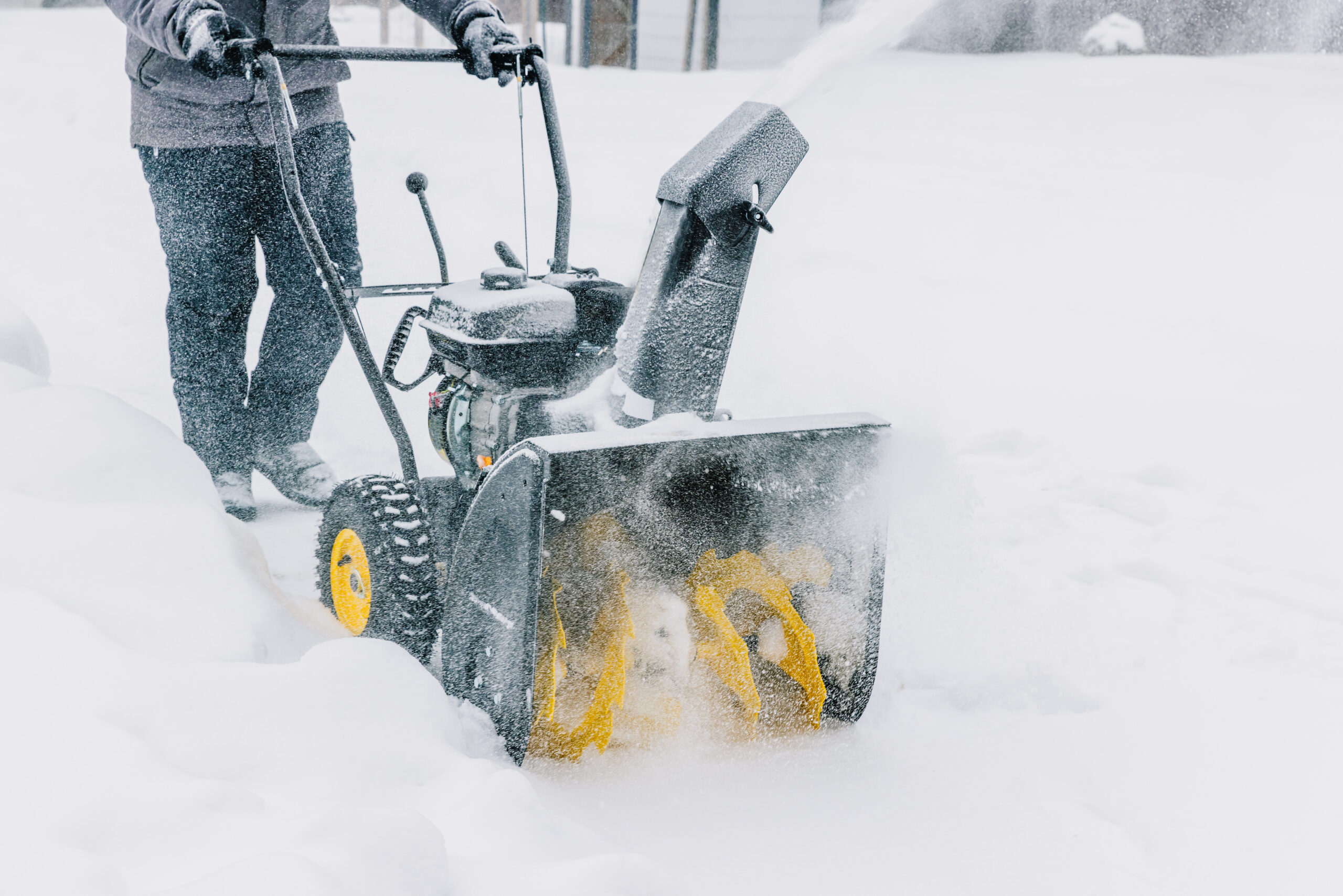 “Man clearing snow with a gas-powered snowblower in a suburban driveway”
